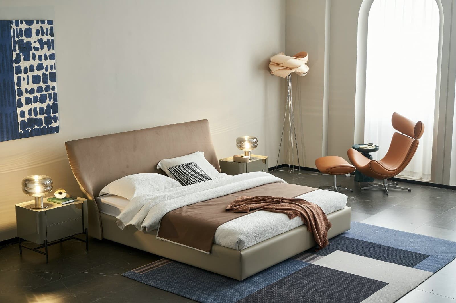 GC1827 upholstered bed in taupe with a curved wing headboard, shown in a bedroom with a tan lounge chair